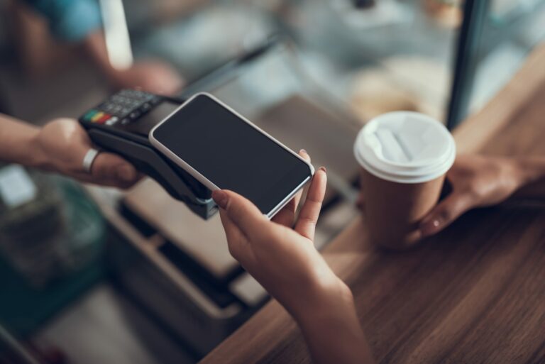 Careful progressive lady with manicure holding her smartphone over the credit card payment machine while using contactless payment system