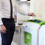 Man in an office throwing plastic bottle into recycling bin for waste management