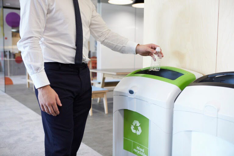 Man in an office throwing plastic bottle into recycling bin for waste management