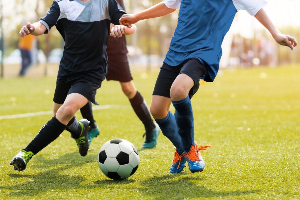 Two soccer players running and kicking a soccer ball. Legs of two young football players on a match. European football youth player legs in action