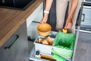 Woman throwing trash into household bins for waste sorting in the kitchen for recycle. Plastic, paper, bio and mixed waste. woman separating food waste bins for simpler recycling
