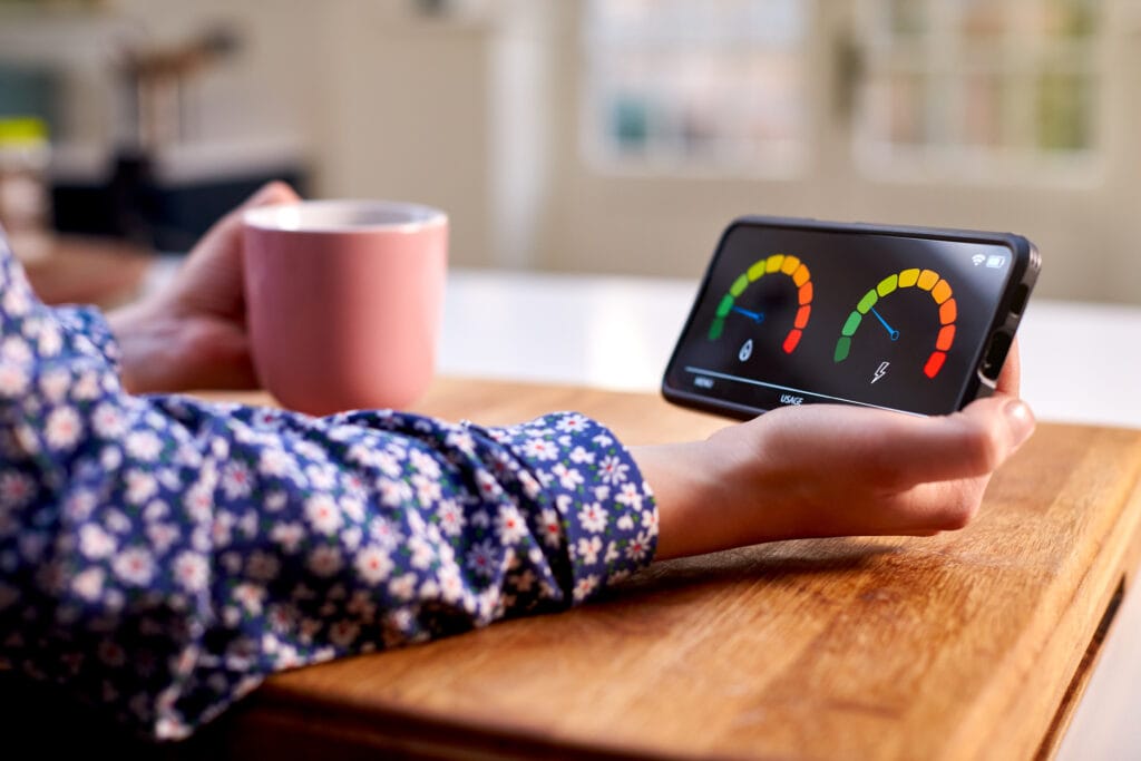 Close Up Of Woman Holding Smart Energy Meter In Kitchen Measuring Domestic Electricity And Gas Use Close Up Of Woman Holding Smart Energy Meter In Kitchen representing july energy price cap