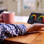 Close Up Of Woman Holding Smart Energy Meter In Kitchen representing july energy price cap