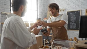 Man paying barista with mobile phone in bakery while holding coffee indoors Man paying barista with mobile phone in bakery while holding coffee representing hospitality