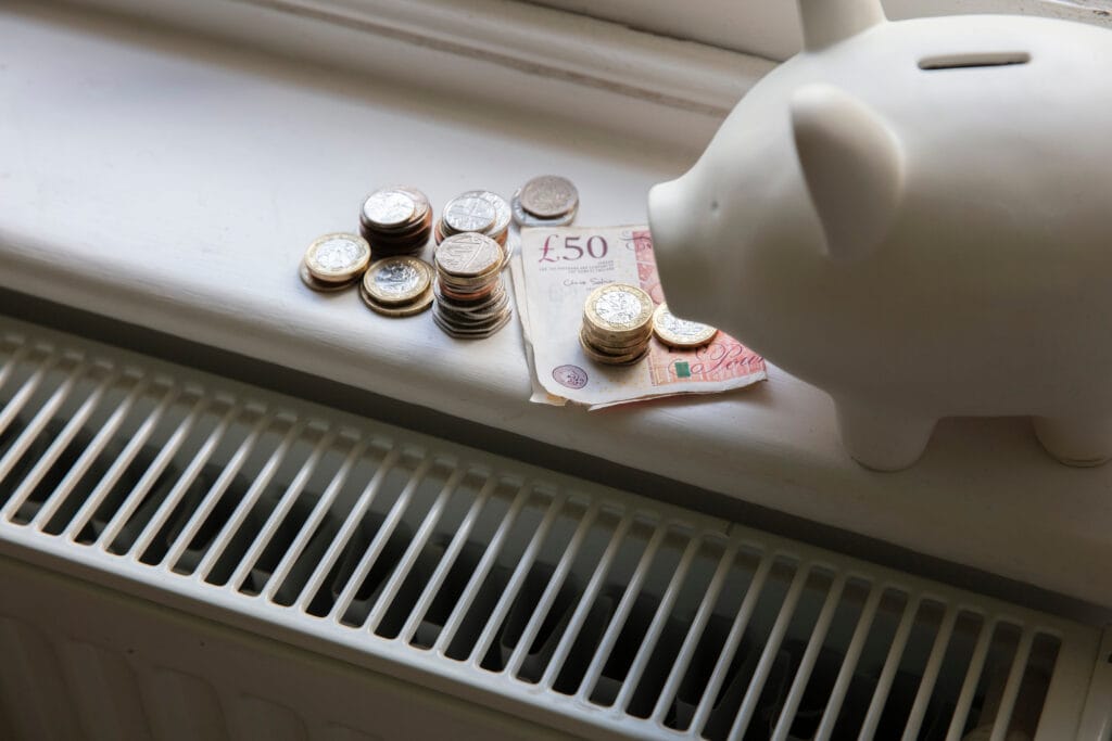 Cost of living crisis. Money on a home radiator heater. Rising cost of energy and bills piggy bank with money on it next to a radiator representing domestic energy bills and the increasing network charge
