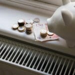 Why Your Energy Bills Are Going Up: The Network Charge Explained 4 piggy bank with money on it next to a radiator representing domestic energy bills and the increasing network charge