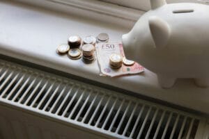 Cost of living crisis. Money on a home radiator heater. Rising cost of energy and bills piggy bank with money on it next to a radiator representing domestic energy bills and the increasing network charge