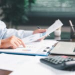 Office businesswoman hand to operate calculator analyzing financial data, counting costs on desk. accounting, financial analysis for business budget planning, calculation support, finance management. bills and calculator in office representing supplier billing issues