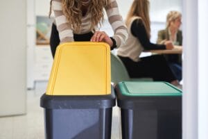 Woman recycling waste in office kitchen with color-coded bins Woman recycling waste in office kitchen with color-coded bins representing waste management