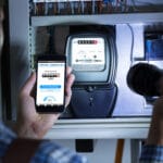 Man's Hand Holding Mobile Phone Showing Electric Meter Reading