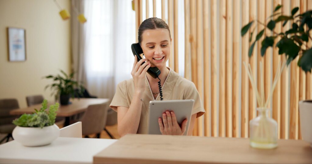 Phone call, spa and woman at reception with tablet checking website for online booking schedule. Consultant, receptionist or girl at front desk on telephone, digital app or appointment at hotel salon woman at aesthetics clinic reception with tablet checking website for online booking schedule.