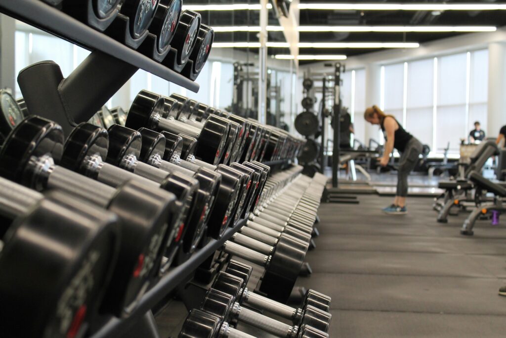 danielle-cerullo-CQfNt66ttZM-unsplash dumbbells in gym with lady exercising in background representing leisure centres