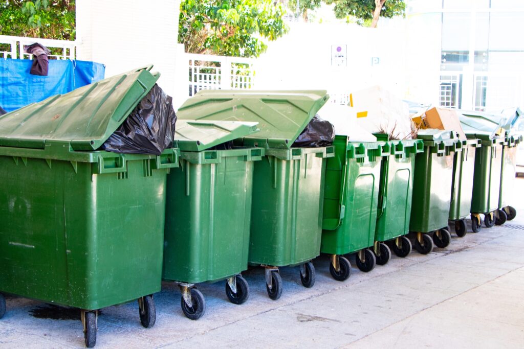 AdobeStock_1851554242 Row of green rubbish bins outdoors representing waste management
