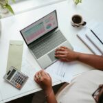 lady researching suppliers on laptop using calculator to decide